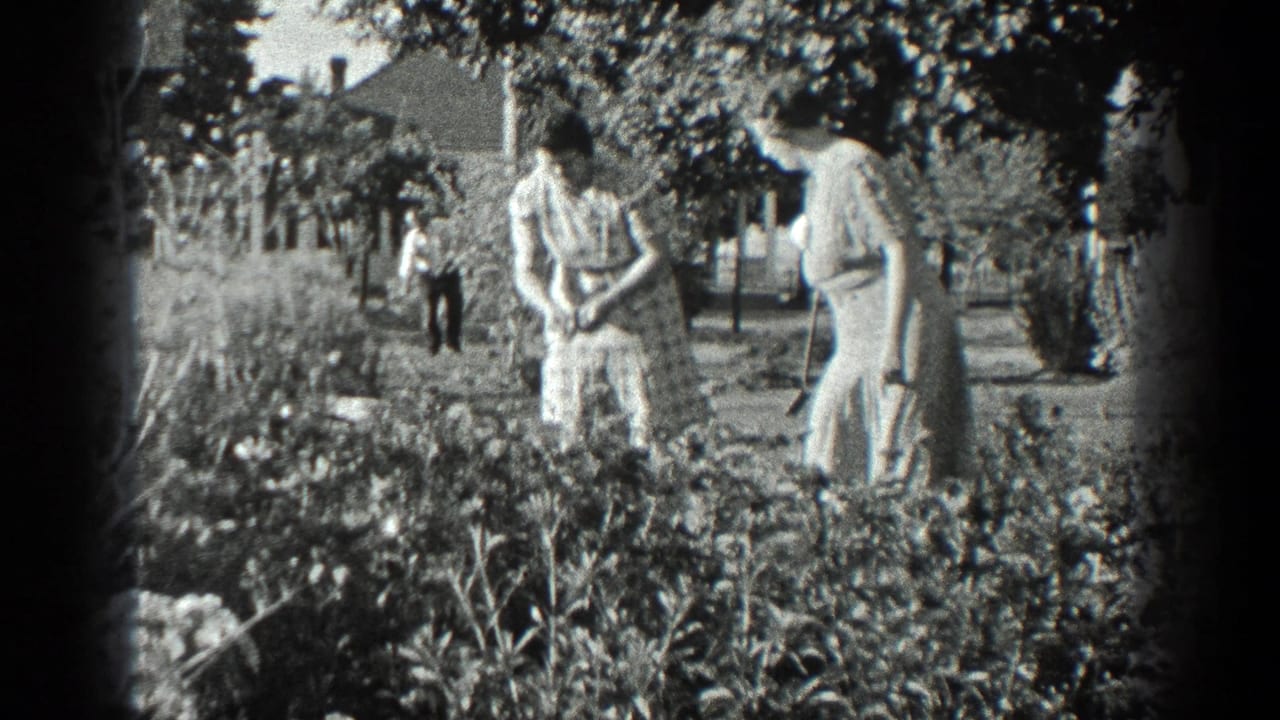Two women stand near garden beds while another figure is visible farther back.