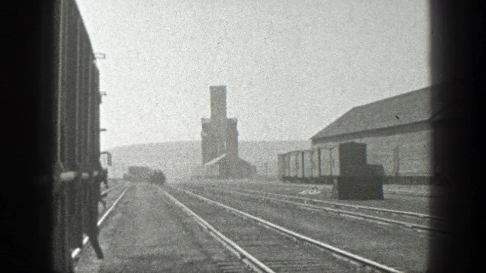 A moving train-view frame shows multiple rail tracks, freight cars, a long building, and a smokestack in California footage dated 1936.