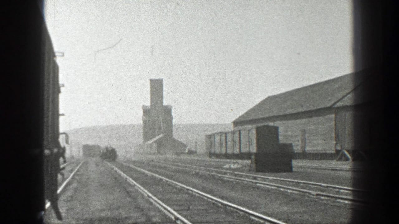 Rail yard view with tracks, freight cars, and a low industrial building.