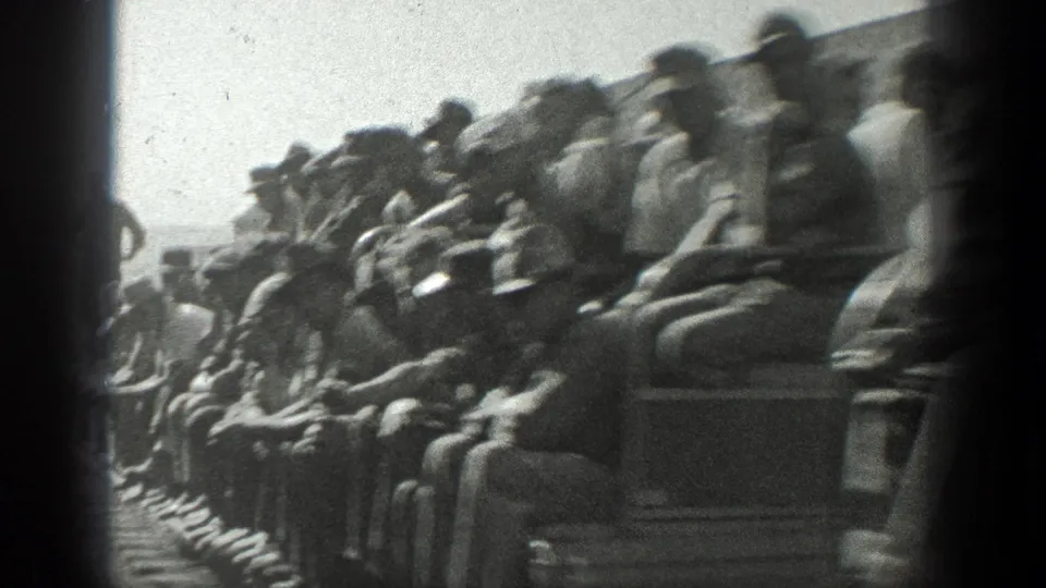 Close 8mm view of adult men packed into open rail cars, with hats and work clothes visible as the train passes.