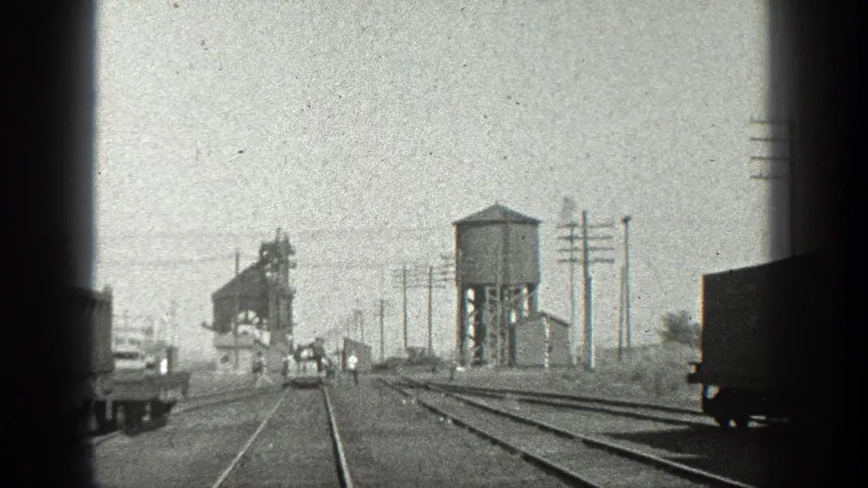 1936 California rail-yard view from a moving train, with tracks, a water tower, industrial equipment, utility poles, and vehicles.