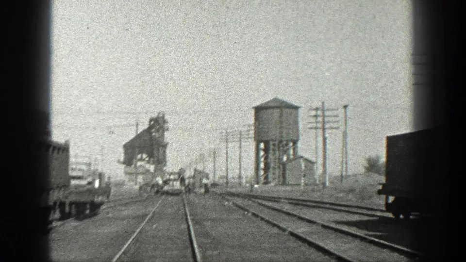 1936 California rail-yard frame with converging tracks, a water tower, industrial structure, freight equipment, and distant workers.