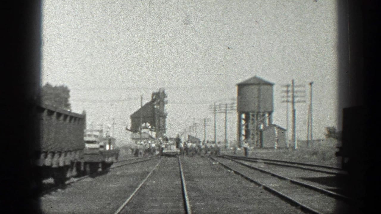 1936 California 8mm view down train tracks toward a water tower, rail cars, utility poles, and people near the line.