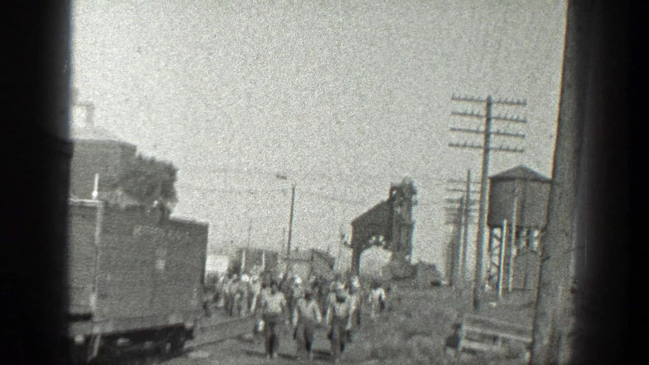 1936 California 8mm frame showing a group of railroad workers moving along tracks in an industrial rail yard setting.