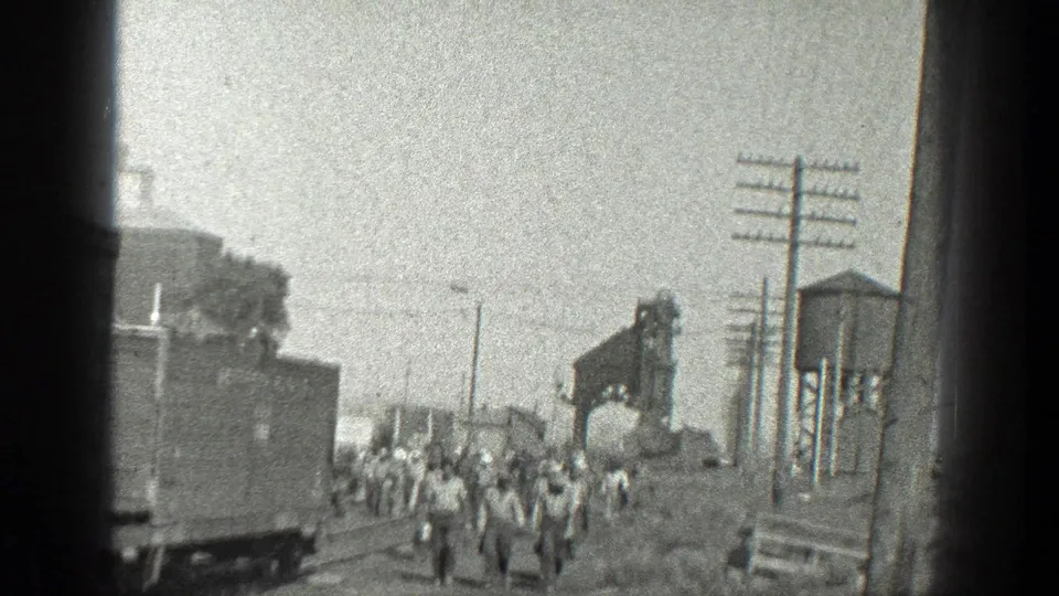 1936 California 8mm frame showing a group of railroad workers moving along tracks in an industrial rail yard setting.