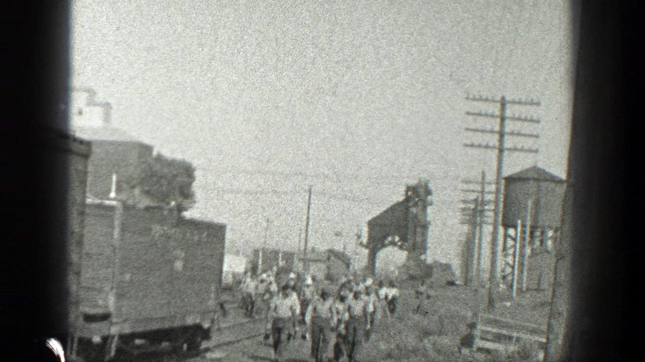 A group of workers walks along tracks beside rail cars and a water tower.