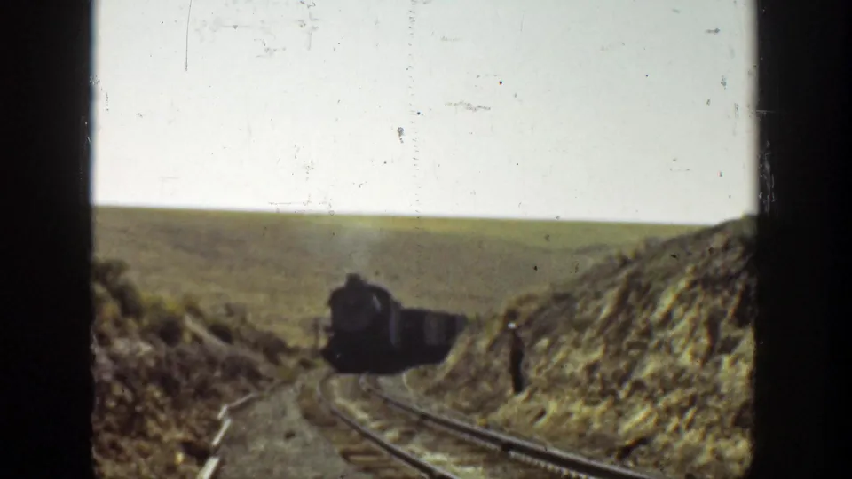 The train nears the camera on a rural California rail curve, framed by dry slopes and 8mm gate edges.