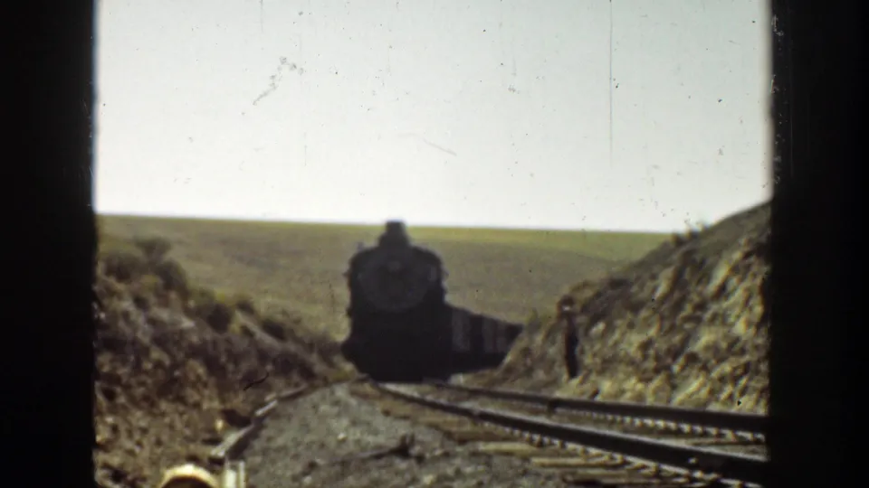 A dark train front approaches on the rails in a 1936 California rural railway scene shot on 8mm film.