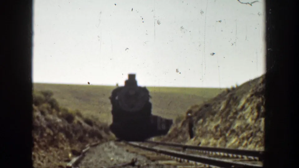 1936 California home-movie frame of a steam locomotive nearing the camera while a small figure stands beside the track cut.