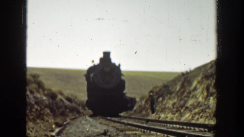 1936 California 8mm frame with the steam locomotive closer to camera, centered between rural embankments and visible film borders.