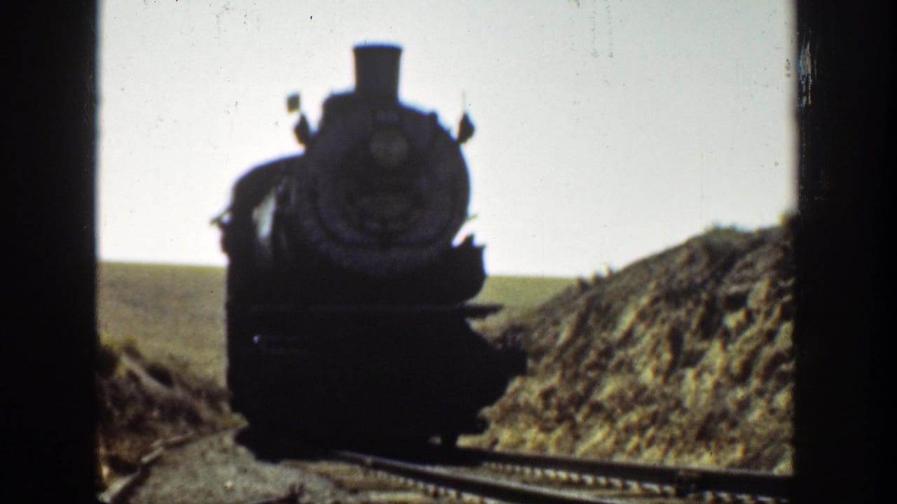 Steam locomotive closer to the camera on tracks through a valley cut.