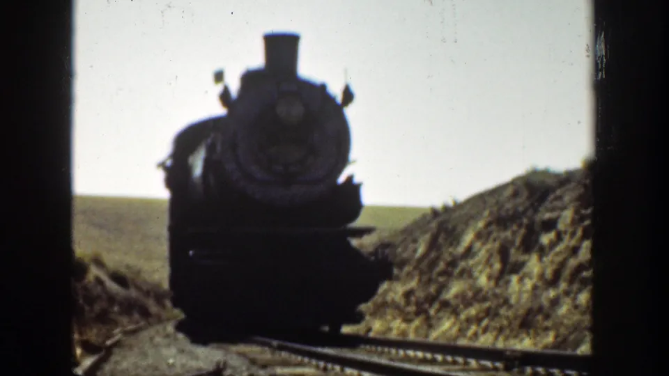The steam locomotive appears nearer on the rails, silhouetted against a bright California sky with earth banks on both sides.