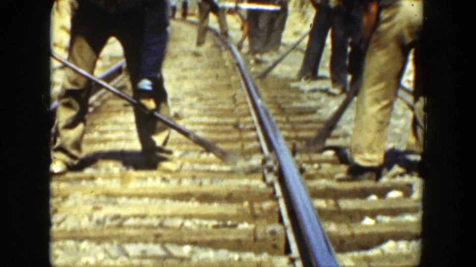 Rail workers in work clothes stand along the track with long tools, appearing to maintain rails and ties in the 1936 California footage.