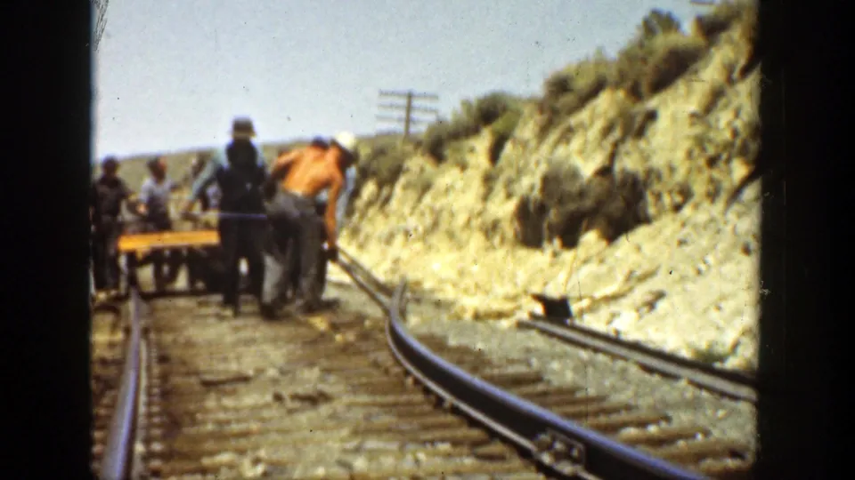 End frame of 1936 California rail repair showing workers, a cart, curved rails, and dry hillside terrain.