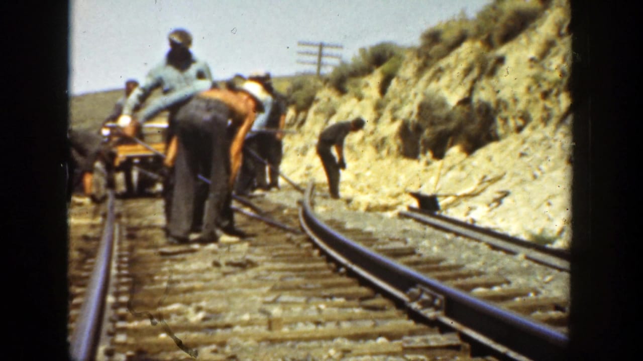 Workers beside railroad tracks on a dry hillside, seen from a moving train.