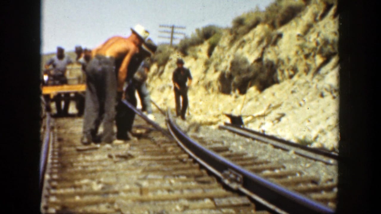 Men work around rails and ties near a rocky railroad cut.