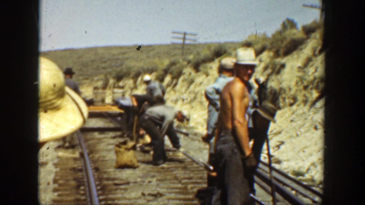 Men working beside railroad tracks in a dry hillside landscape.