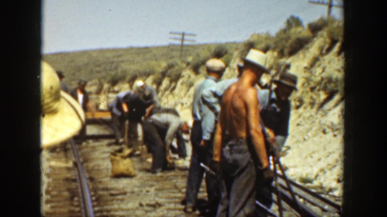 Workers stand and bend near railroad rails on a sunny day.