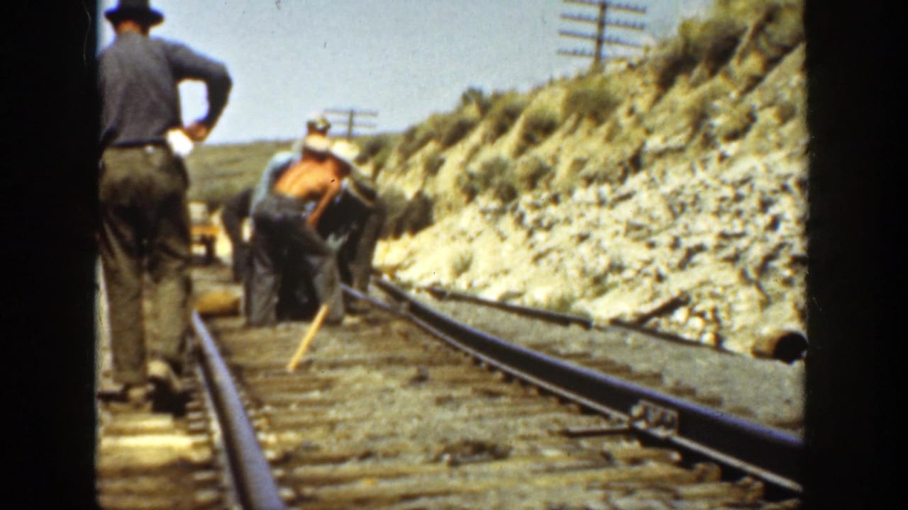 Workers bend over railroad rails while another man stands near the track.