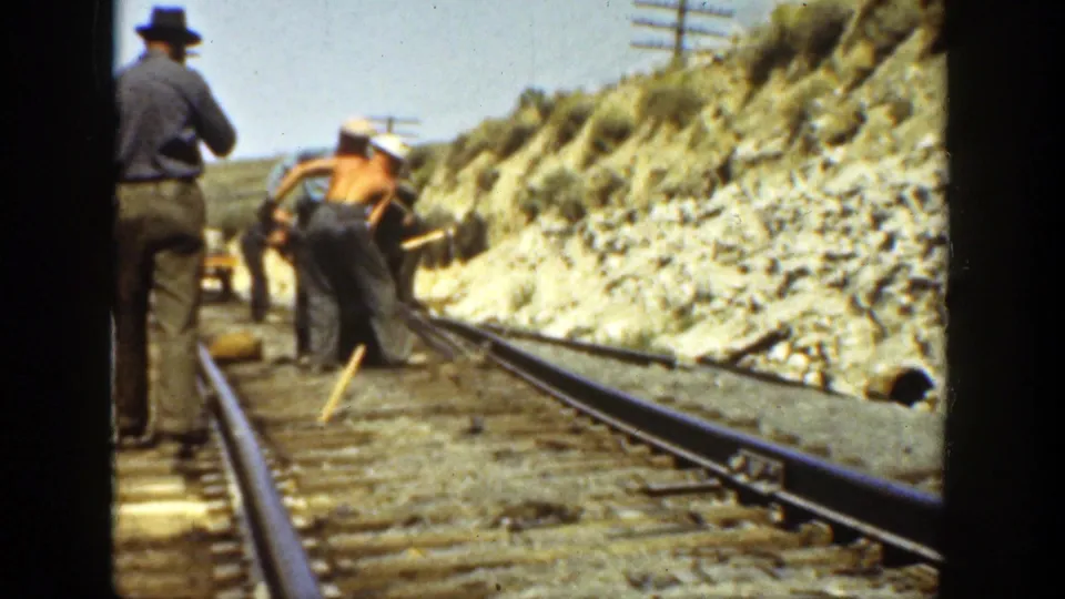 1936 home-movie frame of men working along railroad rails in California, with a rocky embankment, timber ties, and utility poles behind them.