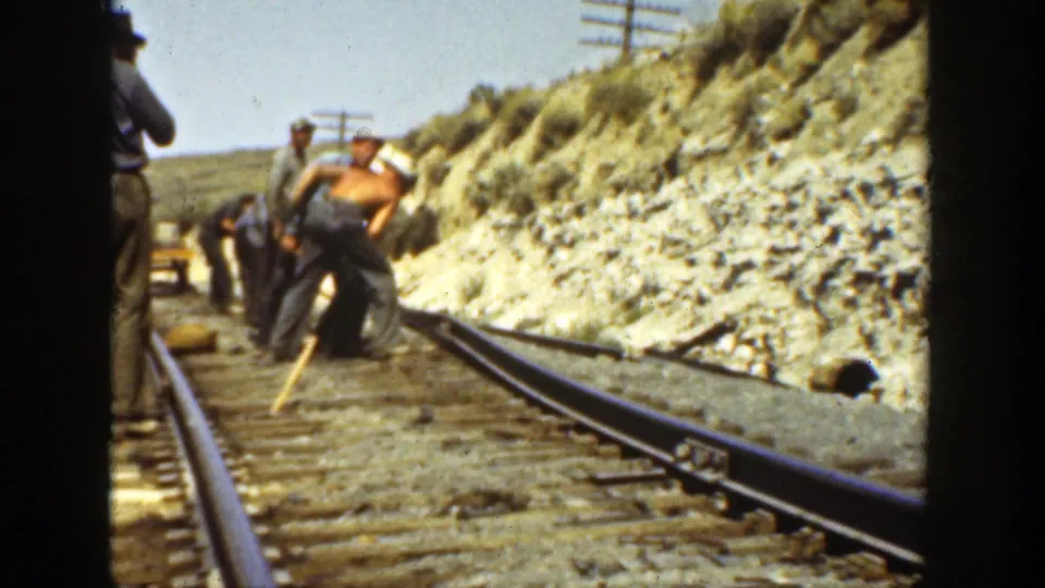 Men continue hand work on railroad rails in 1936 California footage, with rails, ties, tools, and hillside cut banks visible.
