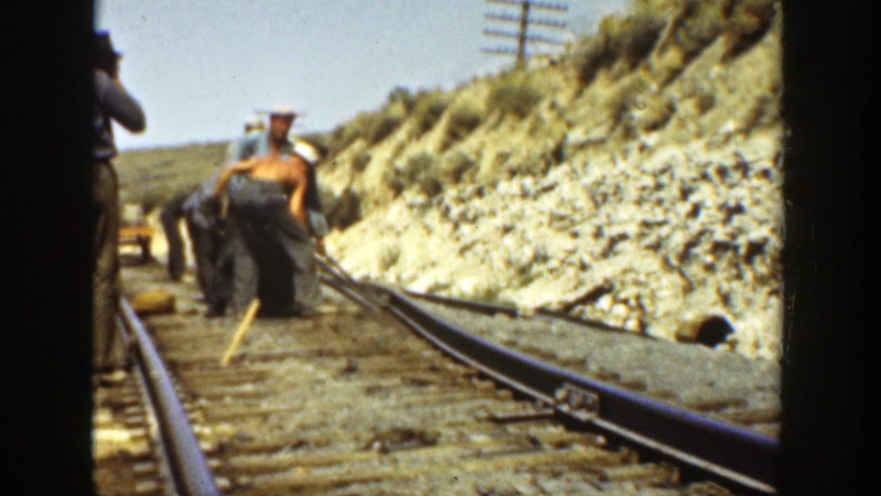 1936 California 8mm frame showing workers along a railway track, with rails, ties, a rocky embankment, and utility poles visible.