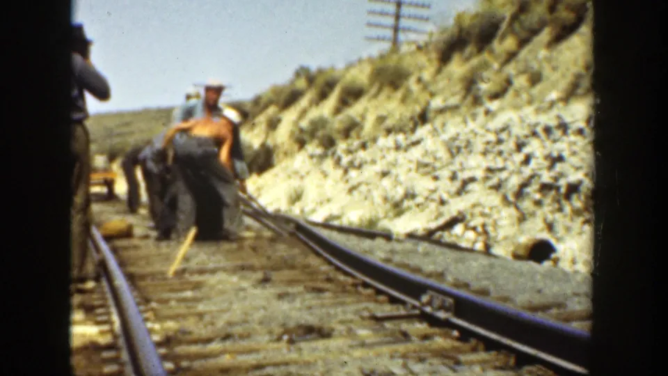 1936 California 8mm frame showing workers along a railway track, with rails, ties, a rocky embankment, and utility poles visible.