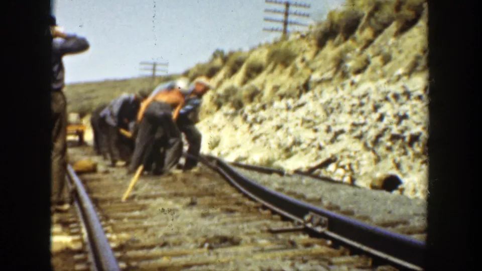 Workers in period work clothes lean over and adjust railway rails in a sunlit California track scene from 1936 metadata.