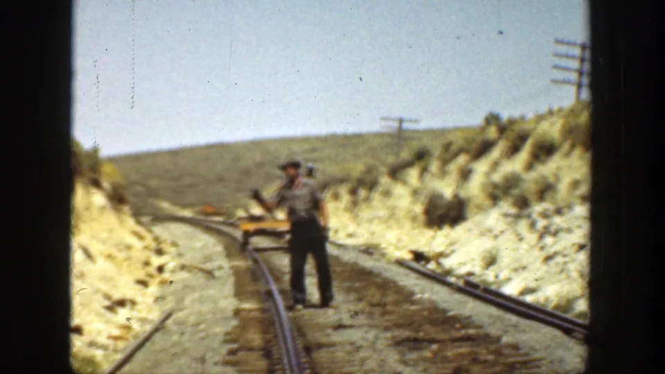 1936 California home-movie frame showing a man standing between rails on a sunlit maintenance section in a dry hillside setting.