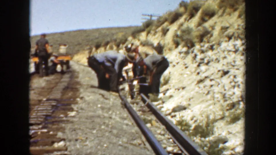 Wider 1936 California view of railroad workers repairing track along a rugged hillside, with a small cart in the background.