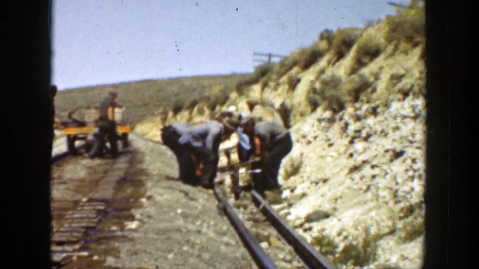 Handheld 8mm view of a small crew working on railroad track in rural California, with rails, ties, ballast, and hillside visible.