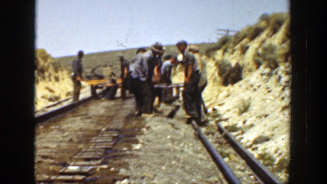 A group of workers gathers around equipment on rails beside dry banks.