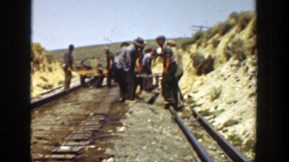 Workers in hats and work clothes gather around equipment on a narrow rail line in the dry California landscape shown in the clip metadata.