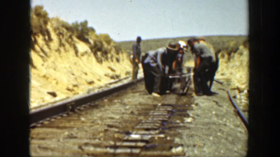 A small crew leans over rail equipment on a narrow track, with dry hillsides and sparse vegetation framing the 1936 California scene.