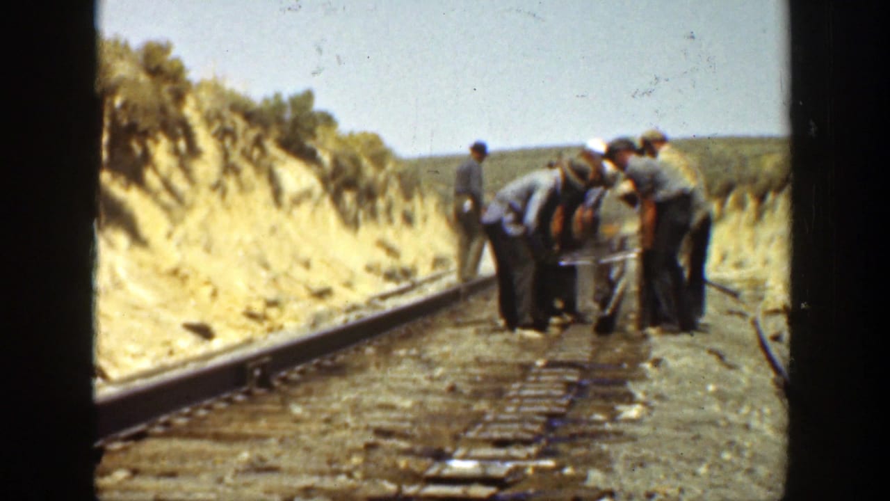 A group of workers stands and bends over equipment on railroad tracks.