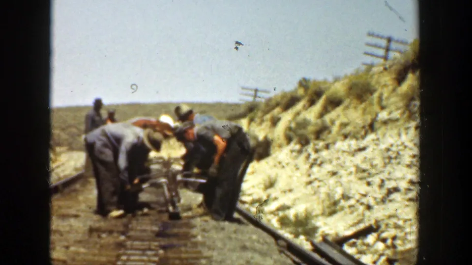 Several railroad workers lean over tools and rail hardware on a rural California track, filmed on 8mm in 1936.