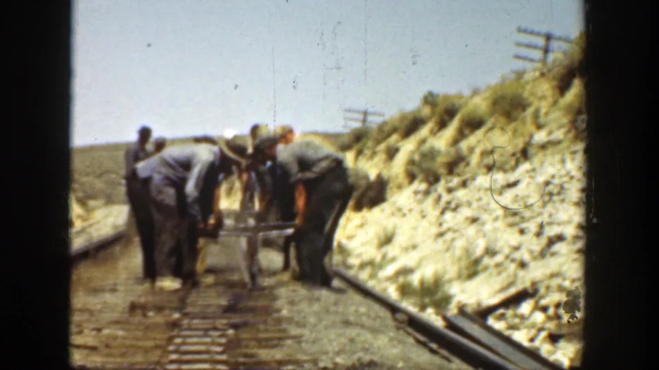 A 1936 California frame shows workers gathered around railroad track tools with rails, ties and a dry hillside visible.