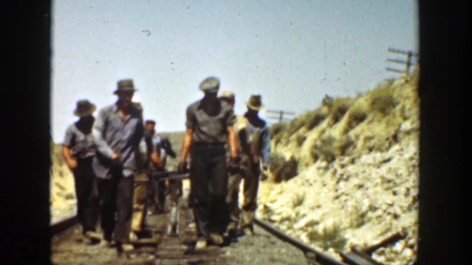 A line of workers walks toward the camera on a California railway track, with tools or rail equipment behind them.