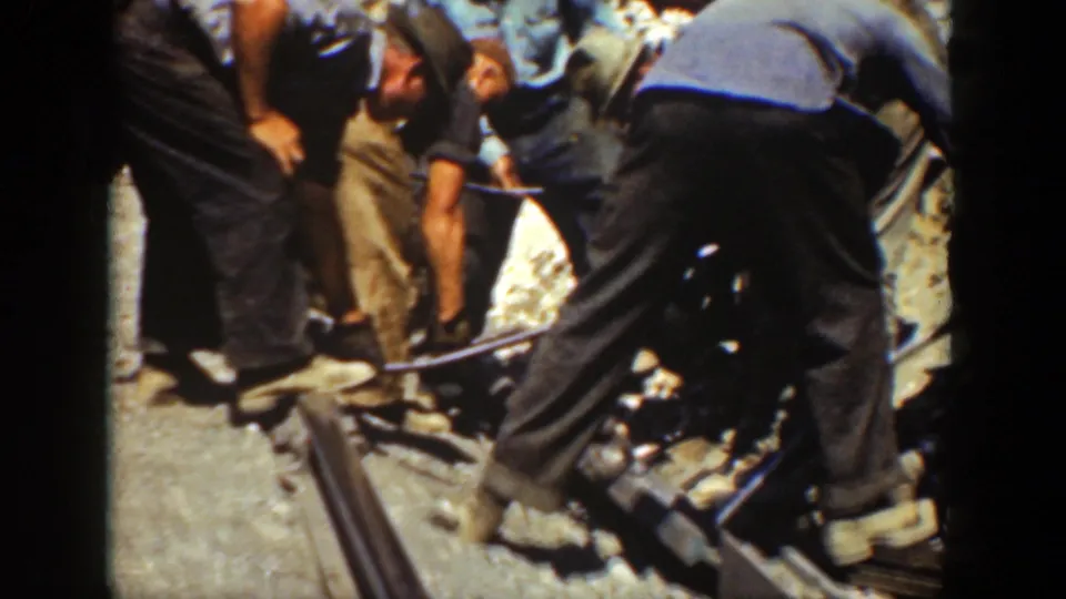 California 1936 frame of men gathered around a rail, using hand tools on a gravel track bed in harsh sunlight.
