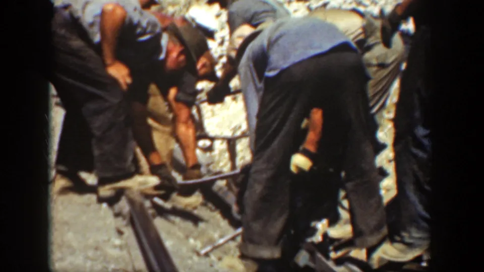 Workers in blue shirts and dark pants cluster beside a rail during apparent track removal or adjustment in California, 1936.