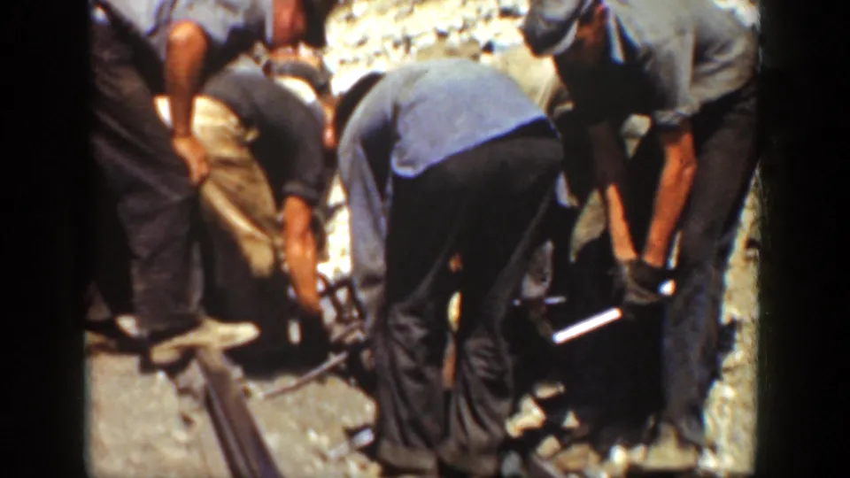Close 8mm view of a railroad work crew around steel rails and tools on a sunlit California track bed in 1936.