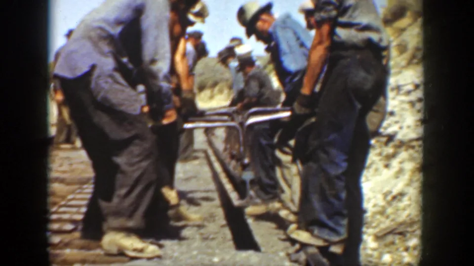 Adult workers in 1936 California appear to align iron rail by hand beside wooden ties on a dry outdoor track bed.