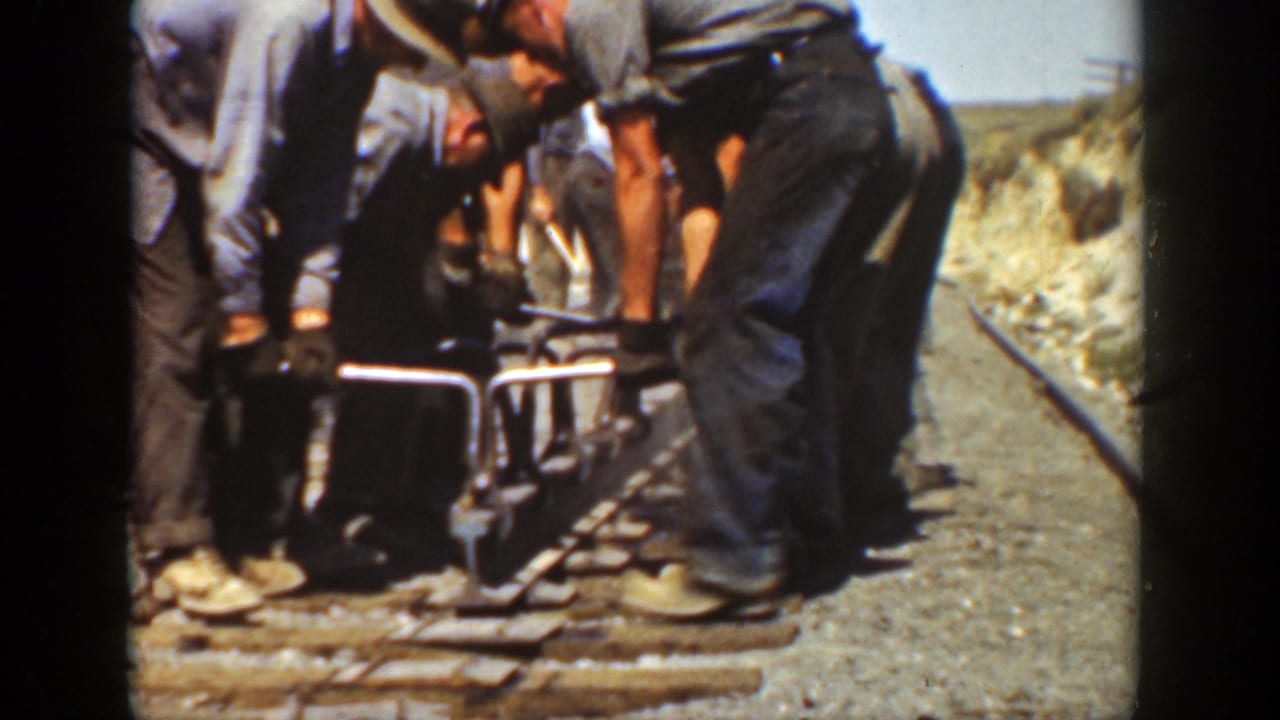 1936 California home-movie frame showing men in work clothes bending over rail hardware on a gravel track bed.