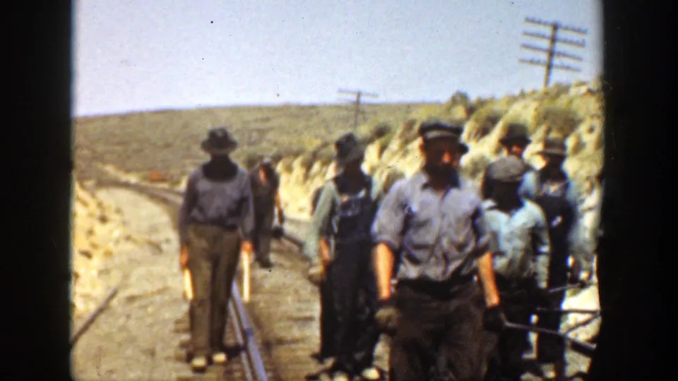 1936 California frame with rail workers in hats standing and walking along track in a sunlit rural cut.