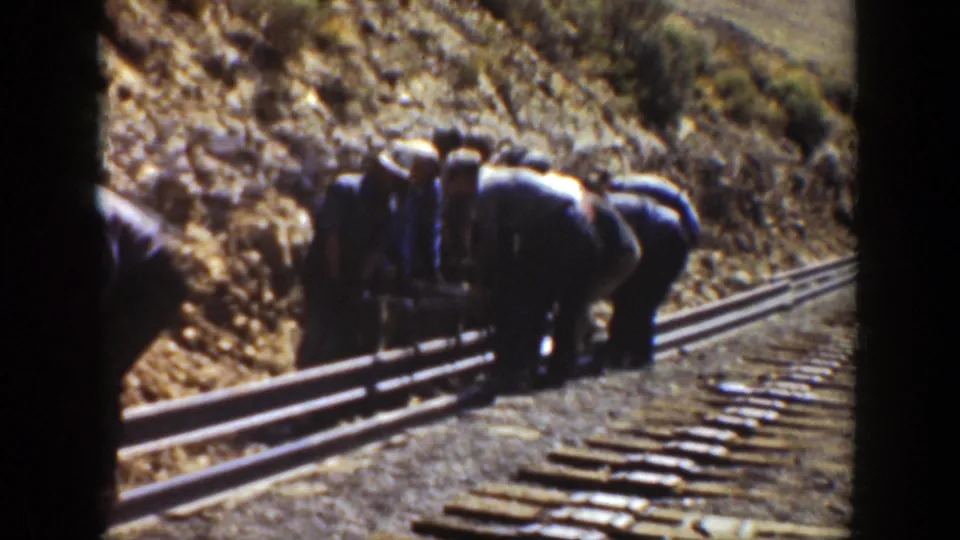 1936 California home-movie frame showing a group of men working over rails and wooden ties in arid terrain.