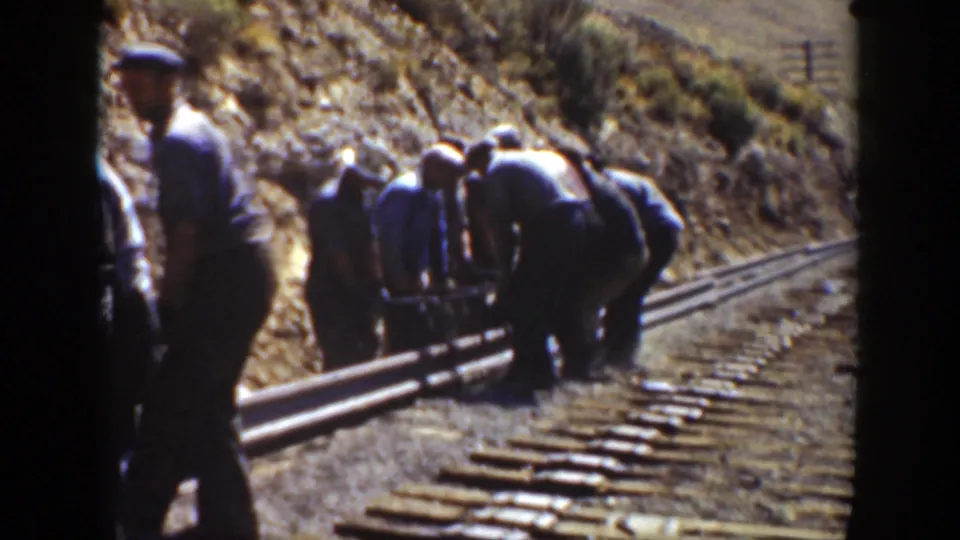 1936 California frame showing a rail crew bent over parallel rails with one worker standing in the foreground.