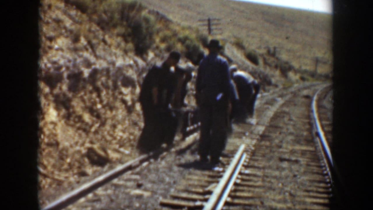Several men stand and bend over a railroad track on a dry hillside.