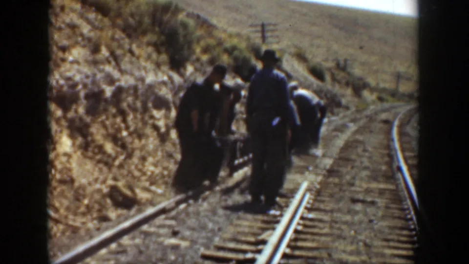 1936 California 8mm frame showing adult men gathered around a rail line beside a dry hillside, viewed from a passing train.