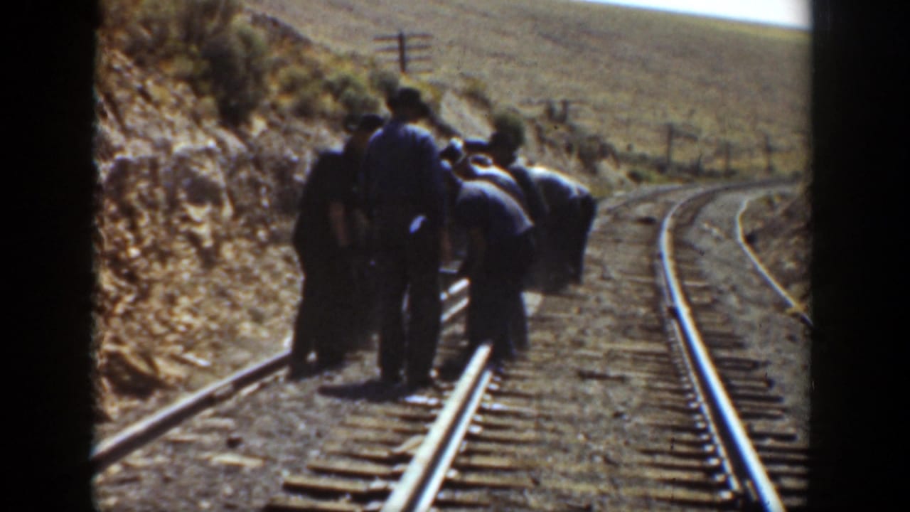 Men cluster along the left rail while the tracks curve through open terrain.