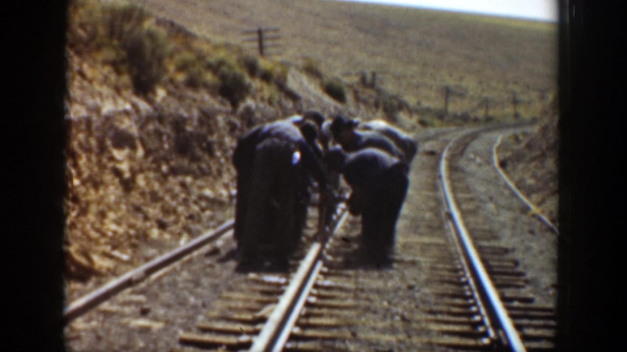 A small work crew leans over the rail line beside a curving track.